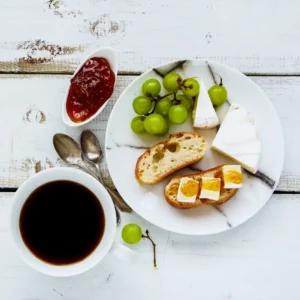 A slice of toasted bread topped with creamy brie cheese and sweet fruit jam, garnished with fresh herbs.