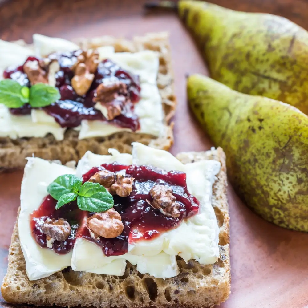 A slice of toasted bread topped with creamy brie cheese and sweet fruit jam, garnished with fresh herbs.