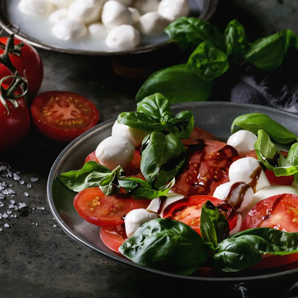 A vibrant Caprese salad with ripe tomatoes, fresh mozzarella, basil leaves, drizzled with olive oil and balsamic glaze.