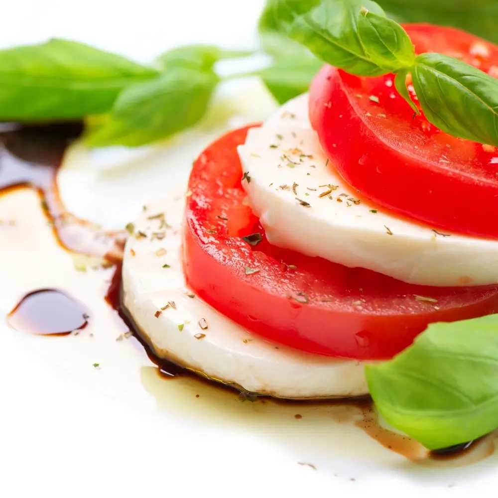 A vibrant Caprese salad with ripe tomatoes, fresh mozzarella, basil leaves, drizzled with olive oil and balsamic glaze.