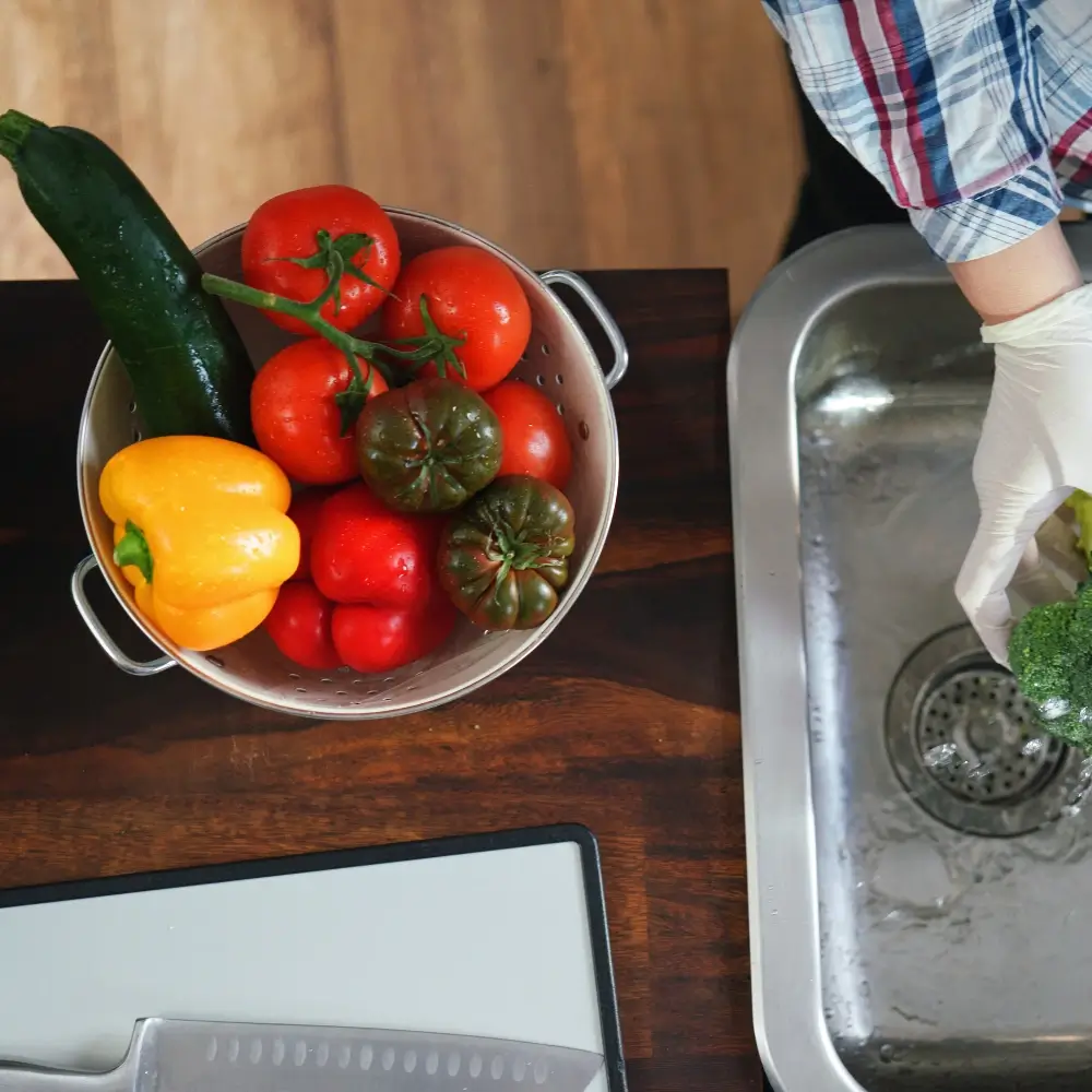 A person using proper food safety techniques, such as washing hands and sanitizing kitchen tools, while preparing fresh ingredients.