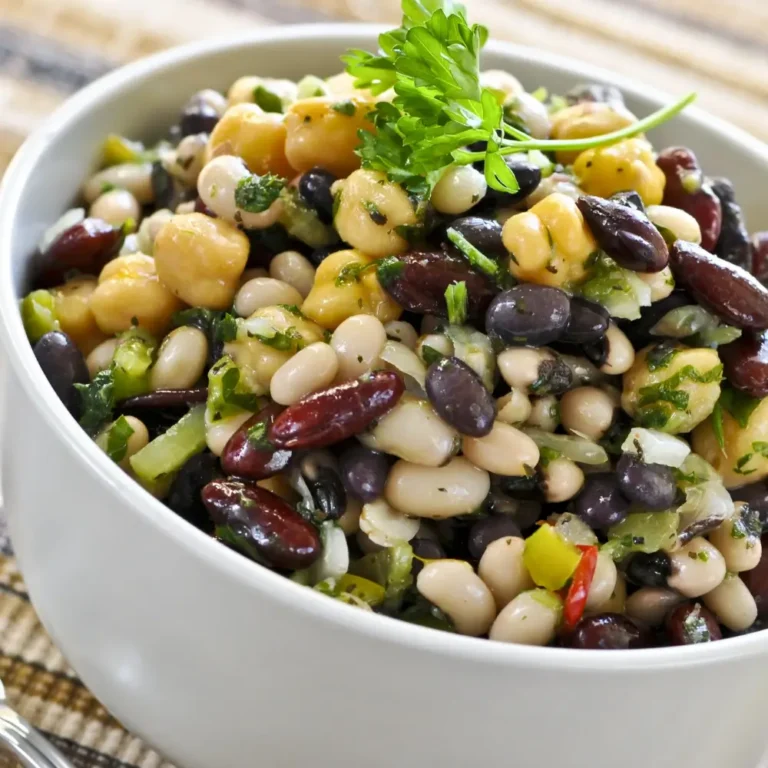 A vibrant bowl of dense bean salad, with a variety of beans, fresh vegetables, and a tangy dressing.