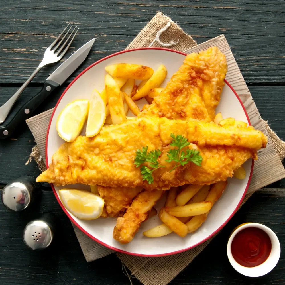 A plate of crispy fried cod fish fillets, golden brown and served with a side of lemon wedges and tartar sauce.