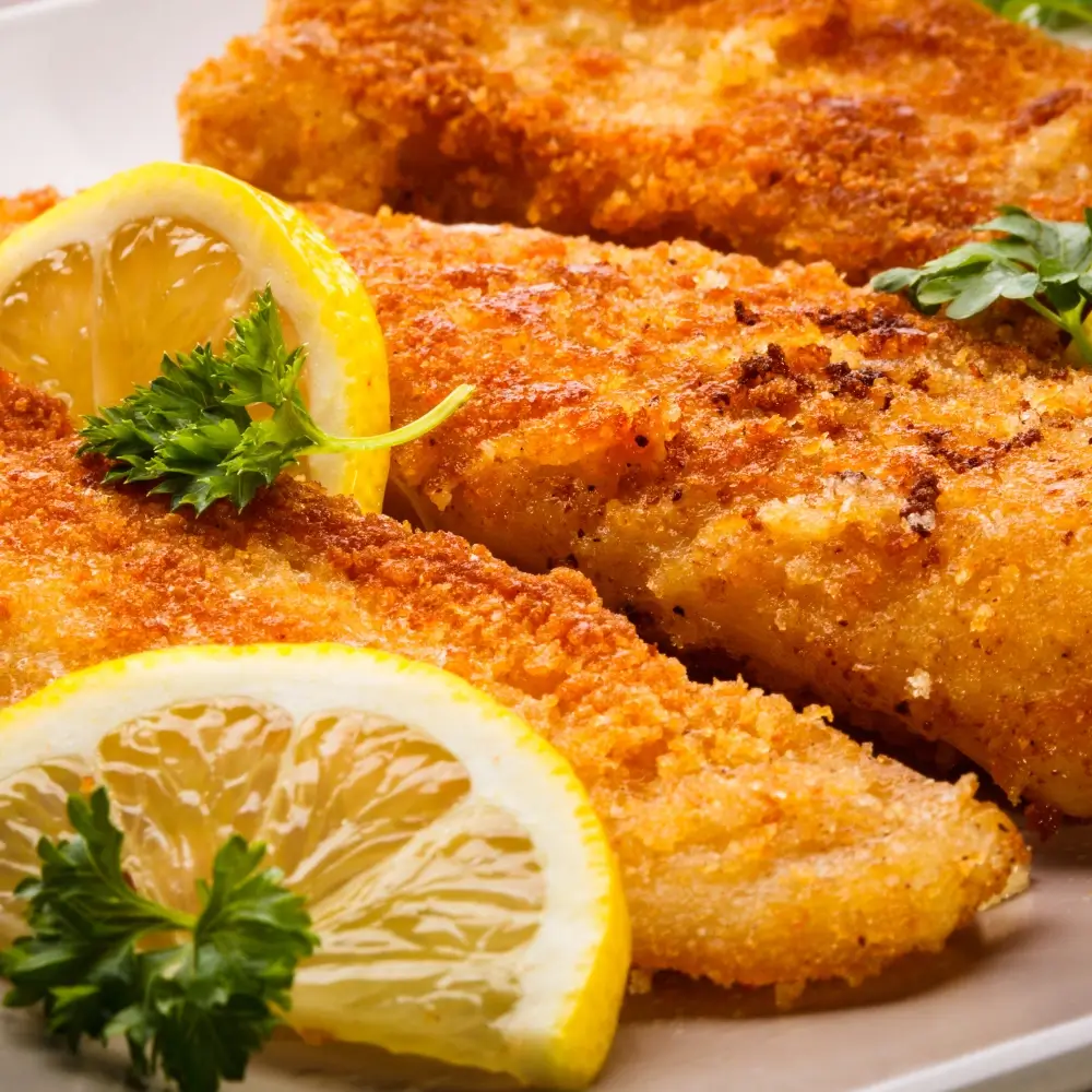 A plate of crispy fried cod fish fillets, golden brown and served with a side of lemon wedges and tartar sauce.