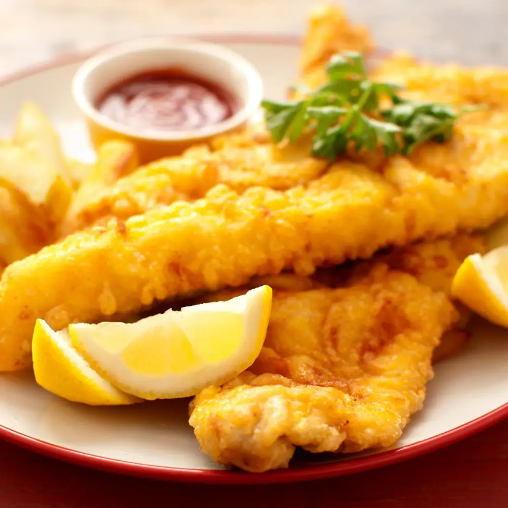 A plate of crispy fried cod fish fillets, golden brown and served with a side of lemon wedges and tartar sauce.