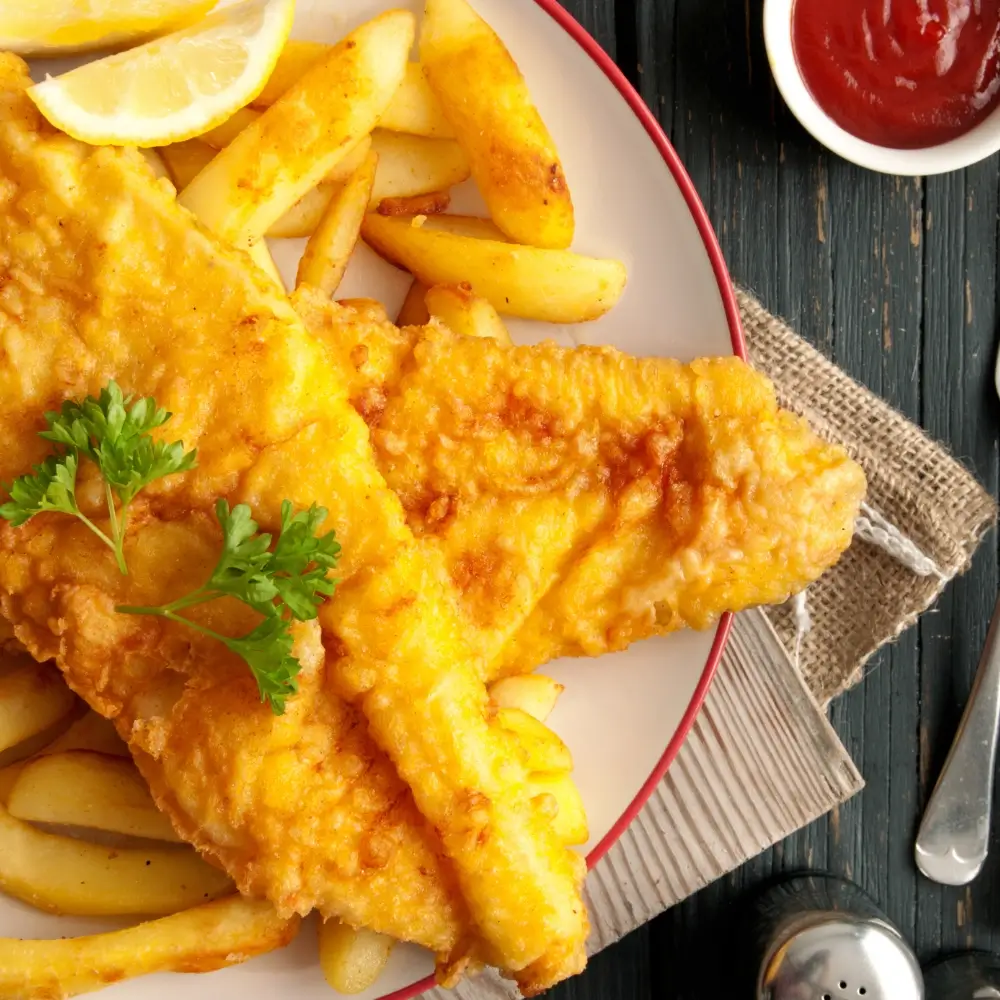 A plate of crispy fried cod fish fillets, golden brown and served with a side of lemon wedges and tartar sauce.