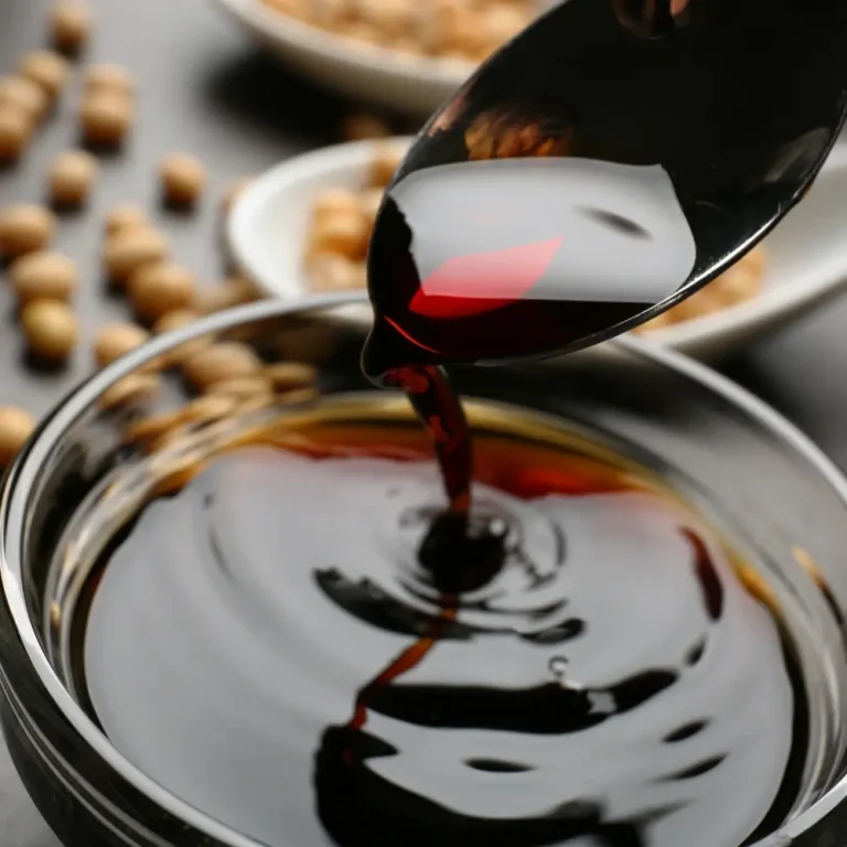 A bottle of homemade soy sauce, rich in color and texture, next to a small dish for serving.