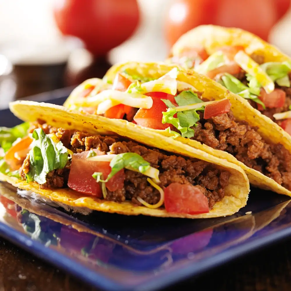 A plate of mouthwatering beef tacos, filled with seasoned ground beef, fresh toppings, and a soft tortilla shell.