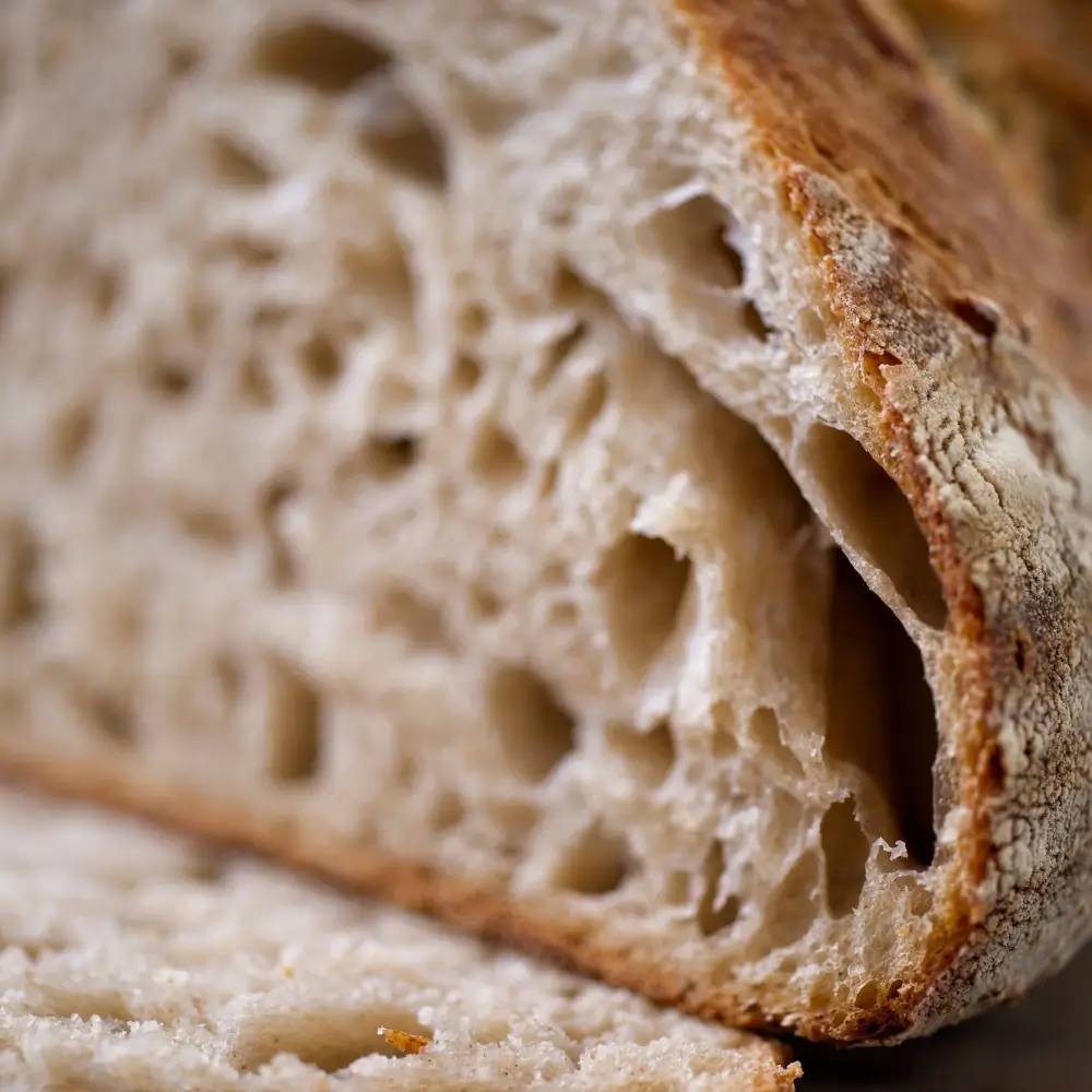 A freshly baked sourdough bread loaf with a golden crust, slightly cracked, showcasing its soft, airy interior.